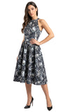 A woman modeling a sleeveless halter-neck midi dress with a black, gray, and white skull and crossbones pattern, paired with black high heels, against a plain white background.